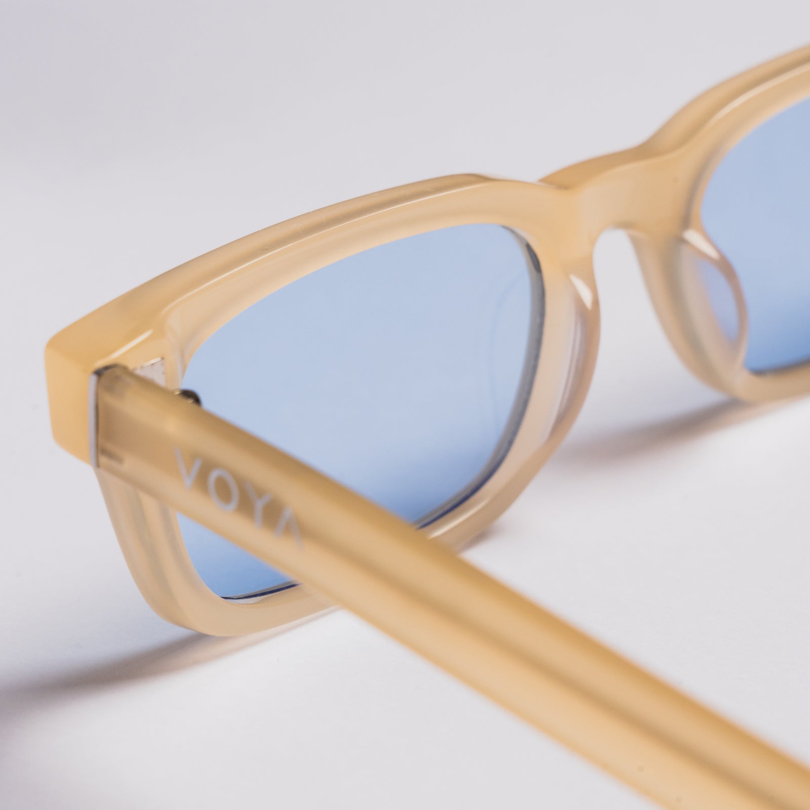 Close-up of VOYA cat-eye sunglasses with translucent beige frames and light blue lenses on a white background.