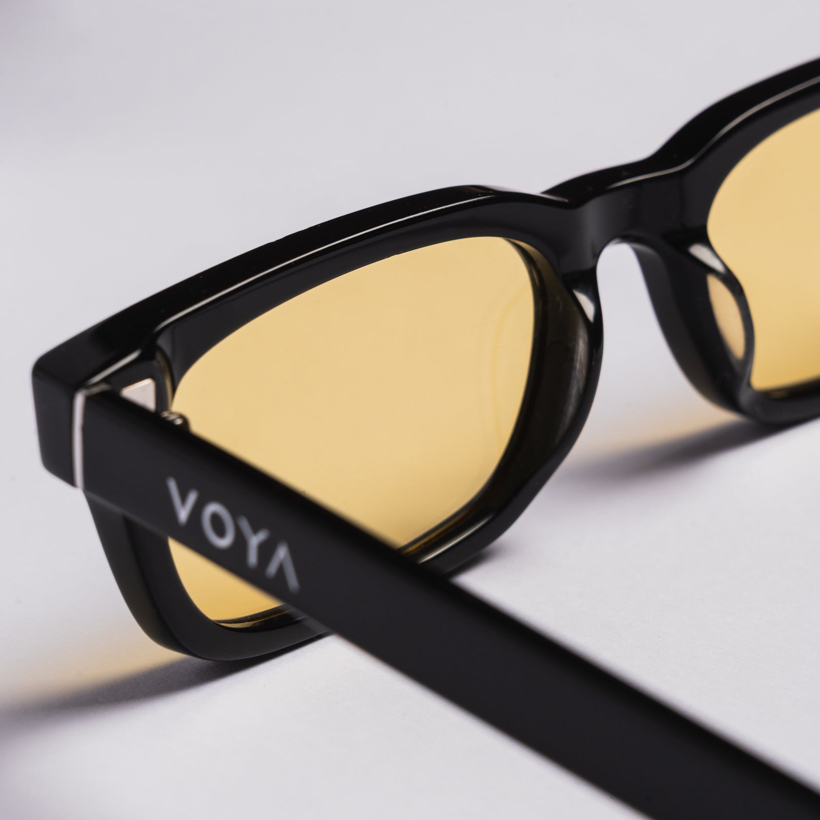 Black rectangular sunglasses with yellow tinted lenses, shown on a clean light gray background. The brand name 'VOYA' is visible on the temple arm.