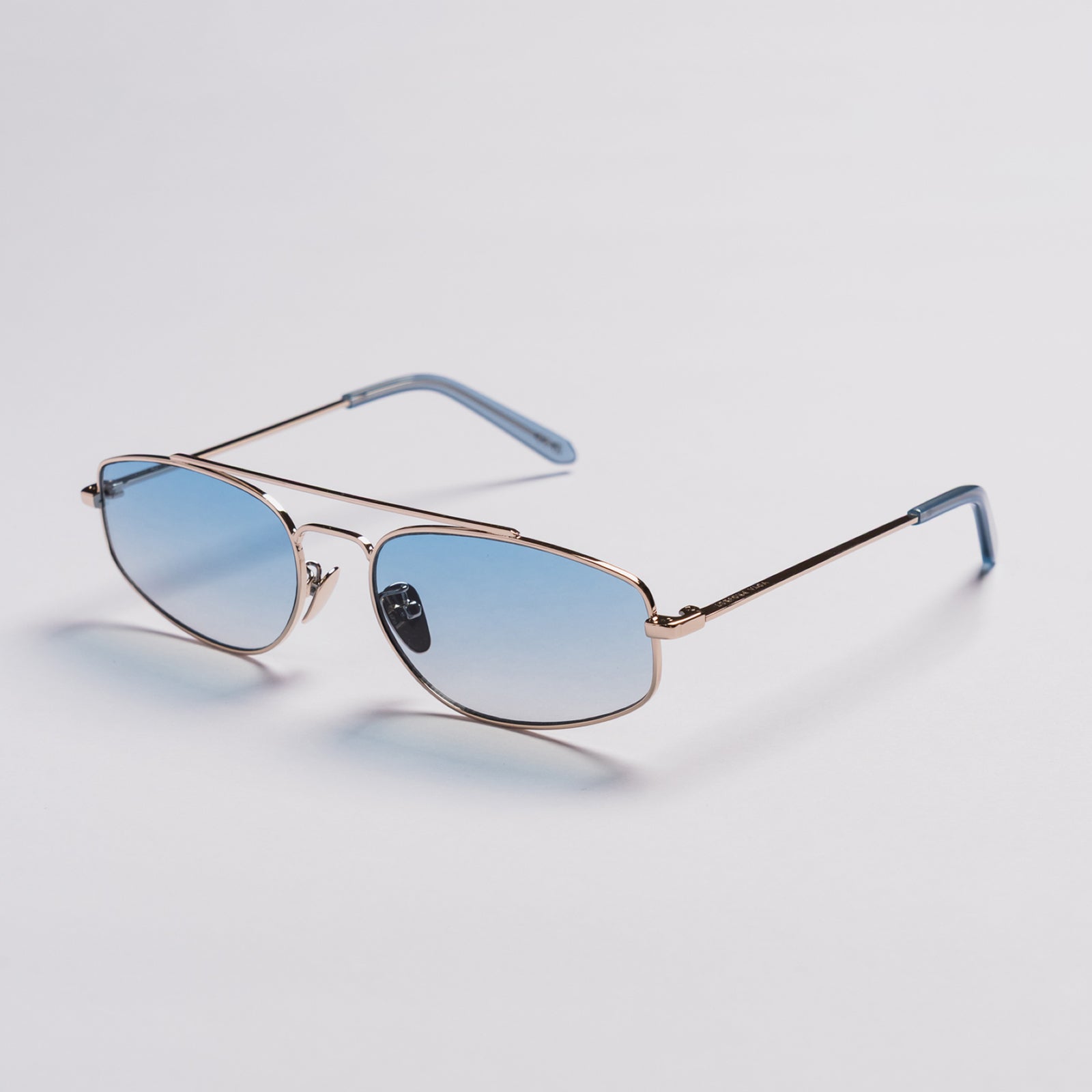 A pair of aviator-style sunglasses with light blue gradient lenses, a thin rose gold metal frame, and light blue temple tips, shown on a light gray background.