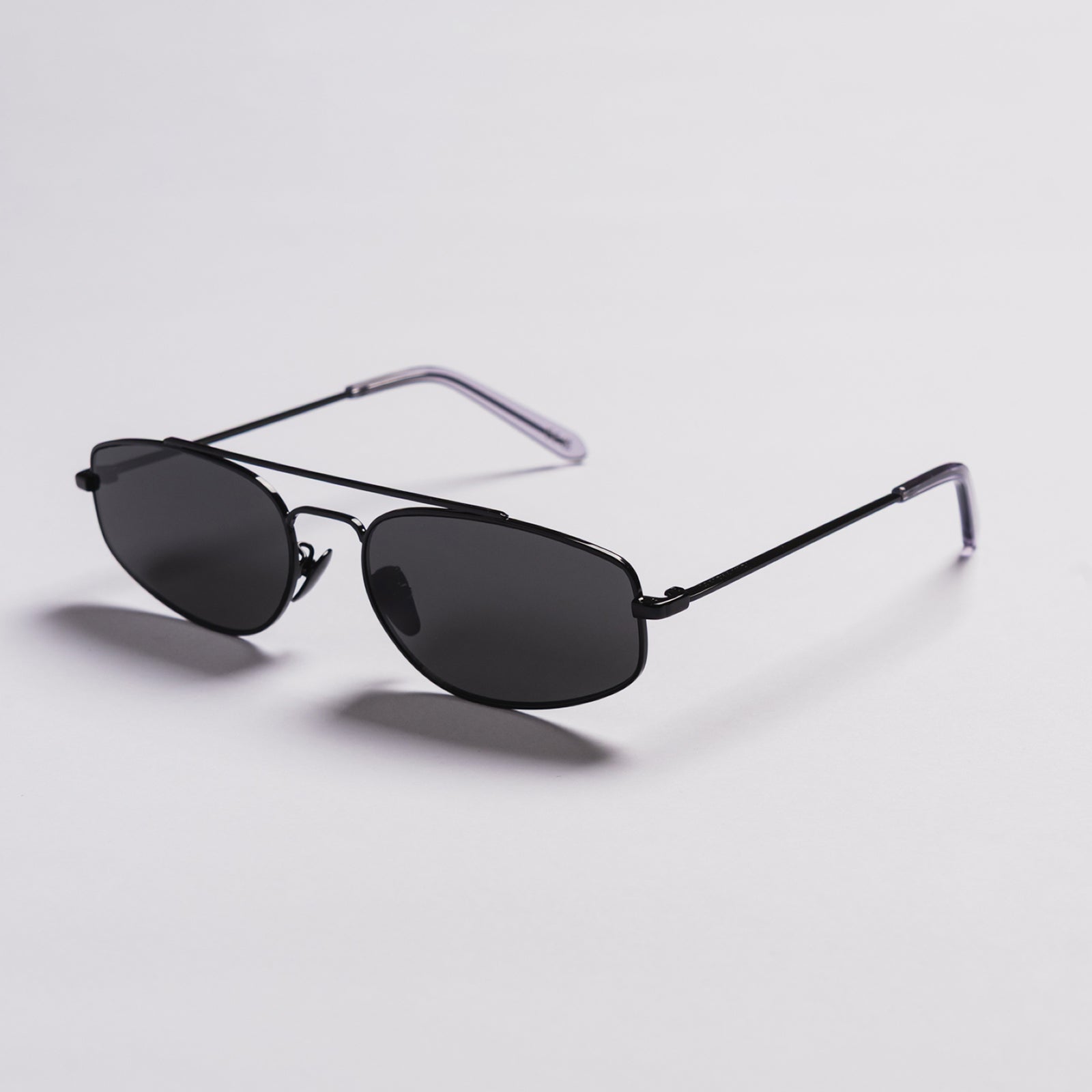 A pair of classic aviator sunglasses with dark gray lenses and a thin black metal frame, featuring translucent purple temple tips, shown on a light gray background.