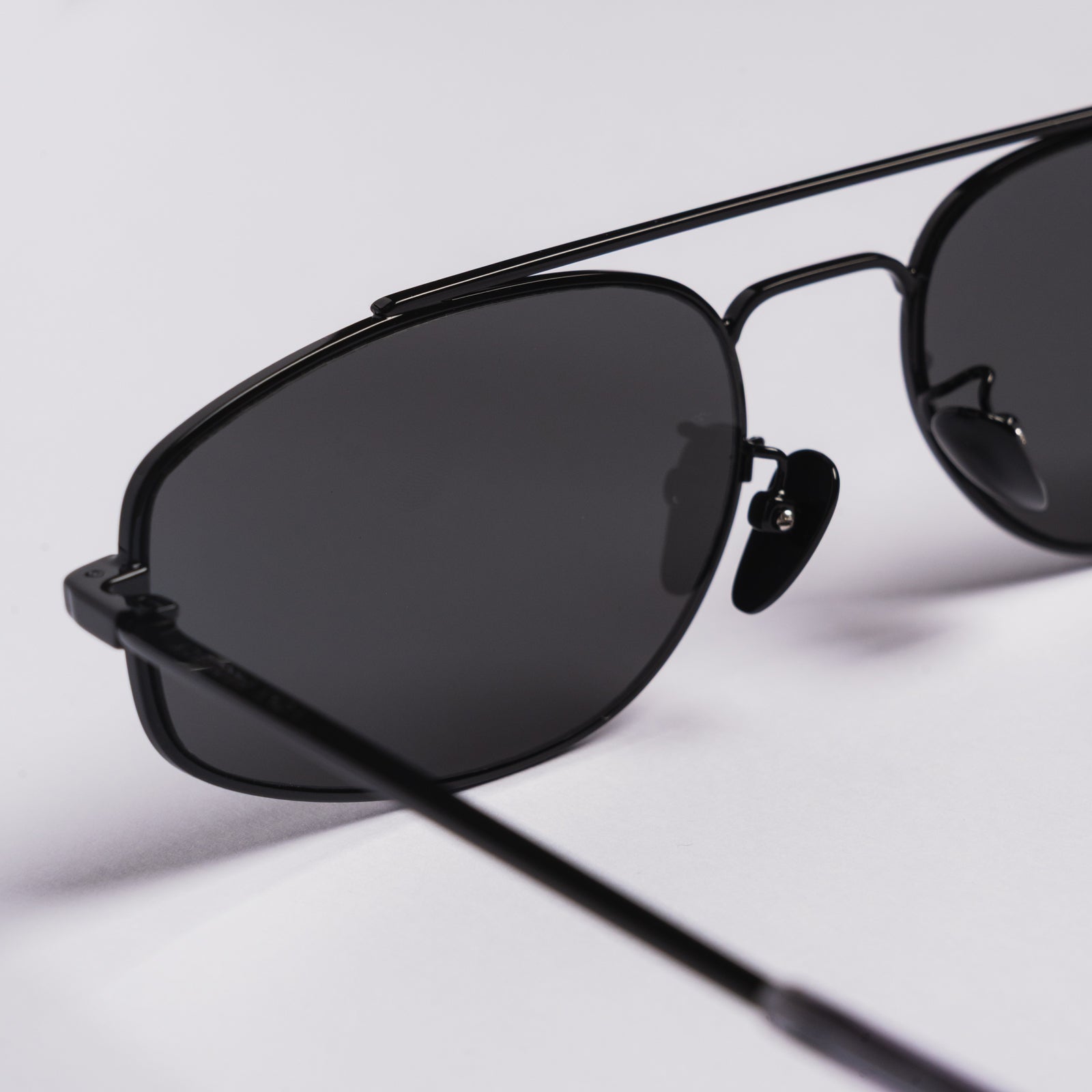 Close-up of black aviator-style sunglasses with dark lenses on a clean white background.