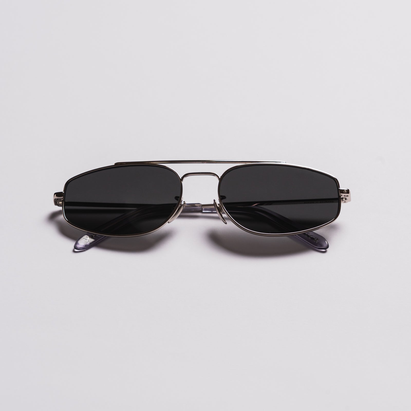 A pair of aviator-style sunglasses with dark lenses, a thin silver metal frame, and temple arms, shown on a light gray background.