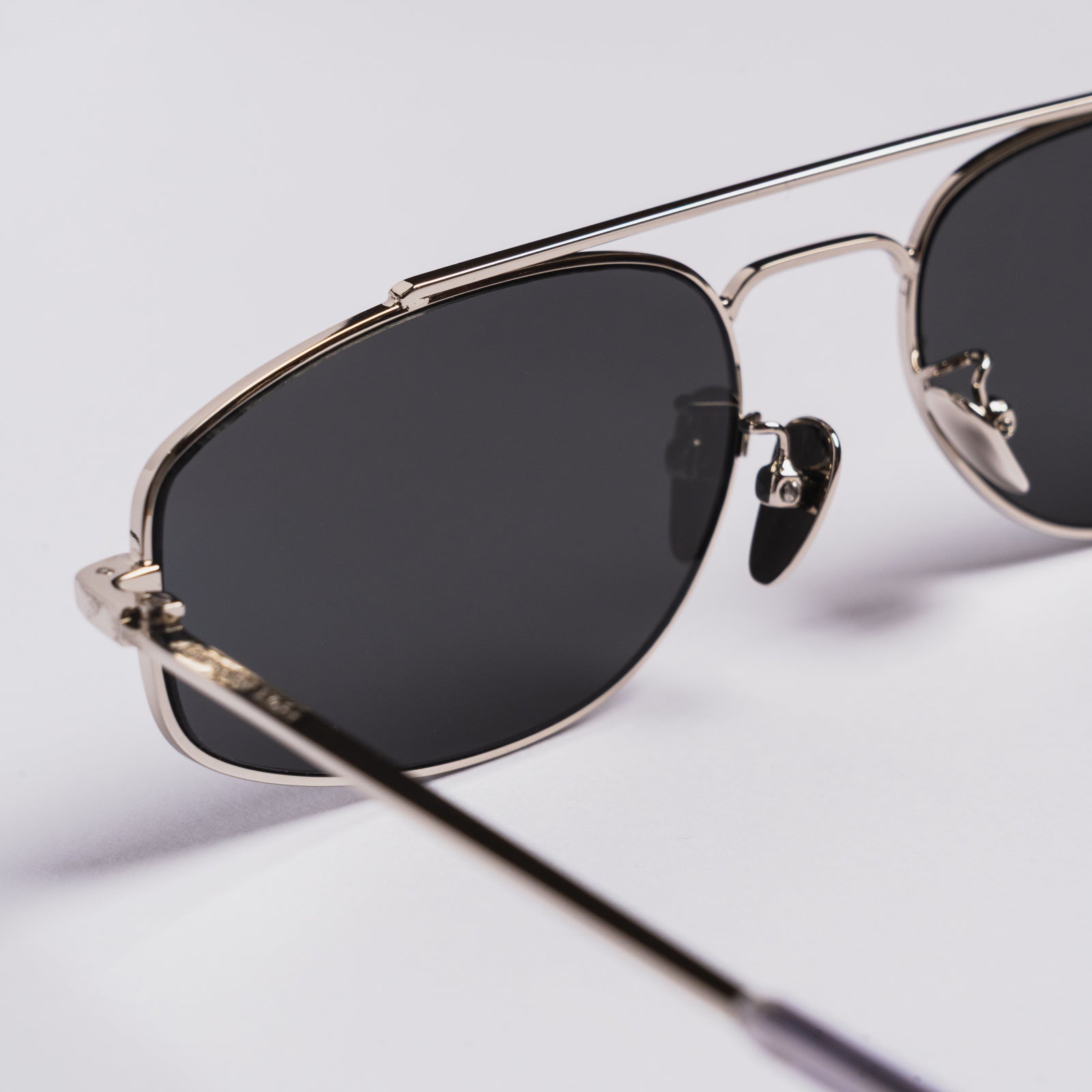Close-up of aviator-style sunglasses with a thin silver metal frame and dark tinted lenses on a light gray background.