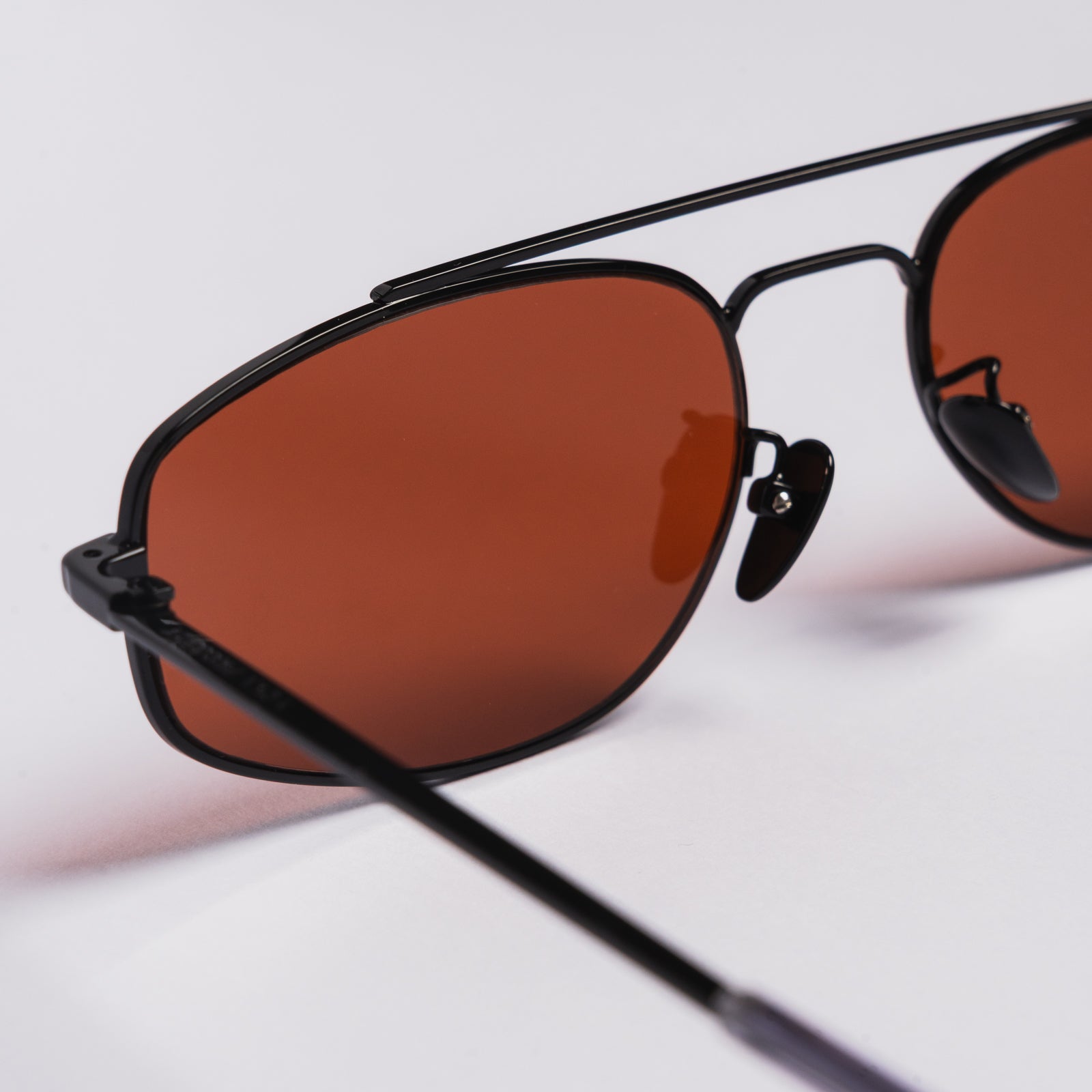 Close-up of black aviator-style sunglasses with warm brown tinted lenses on a clean white background.
