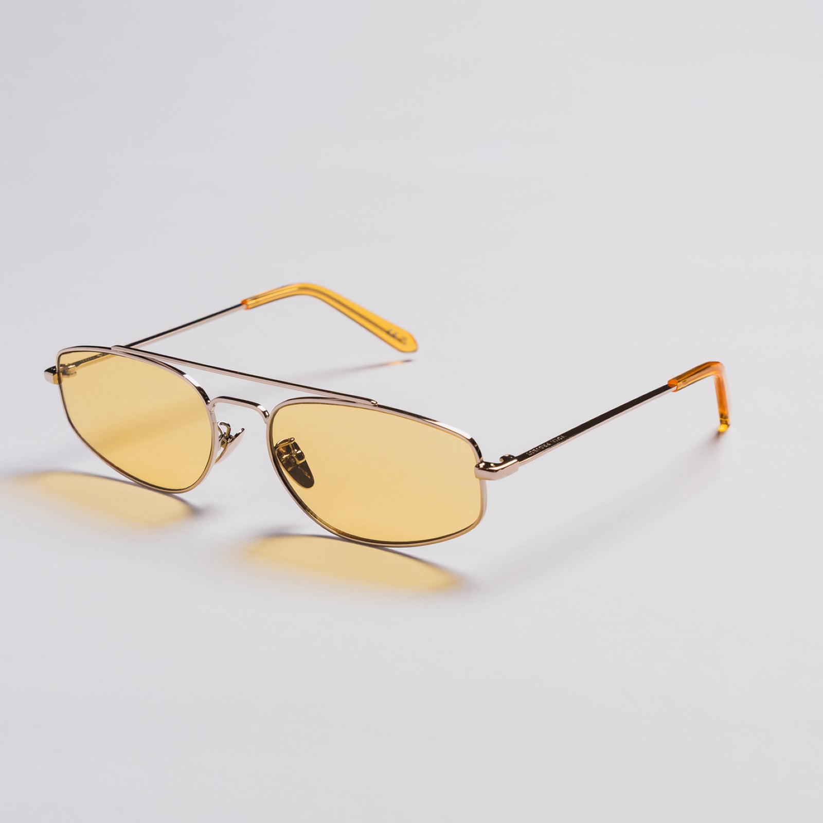 A pair of aviator-style sunglasses with yellow tinted lenses and a thin gold metal frame, displayed on a clean light gray background.
