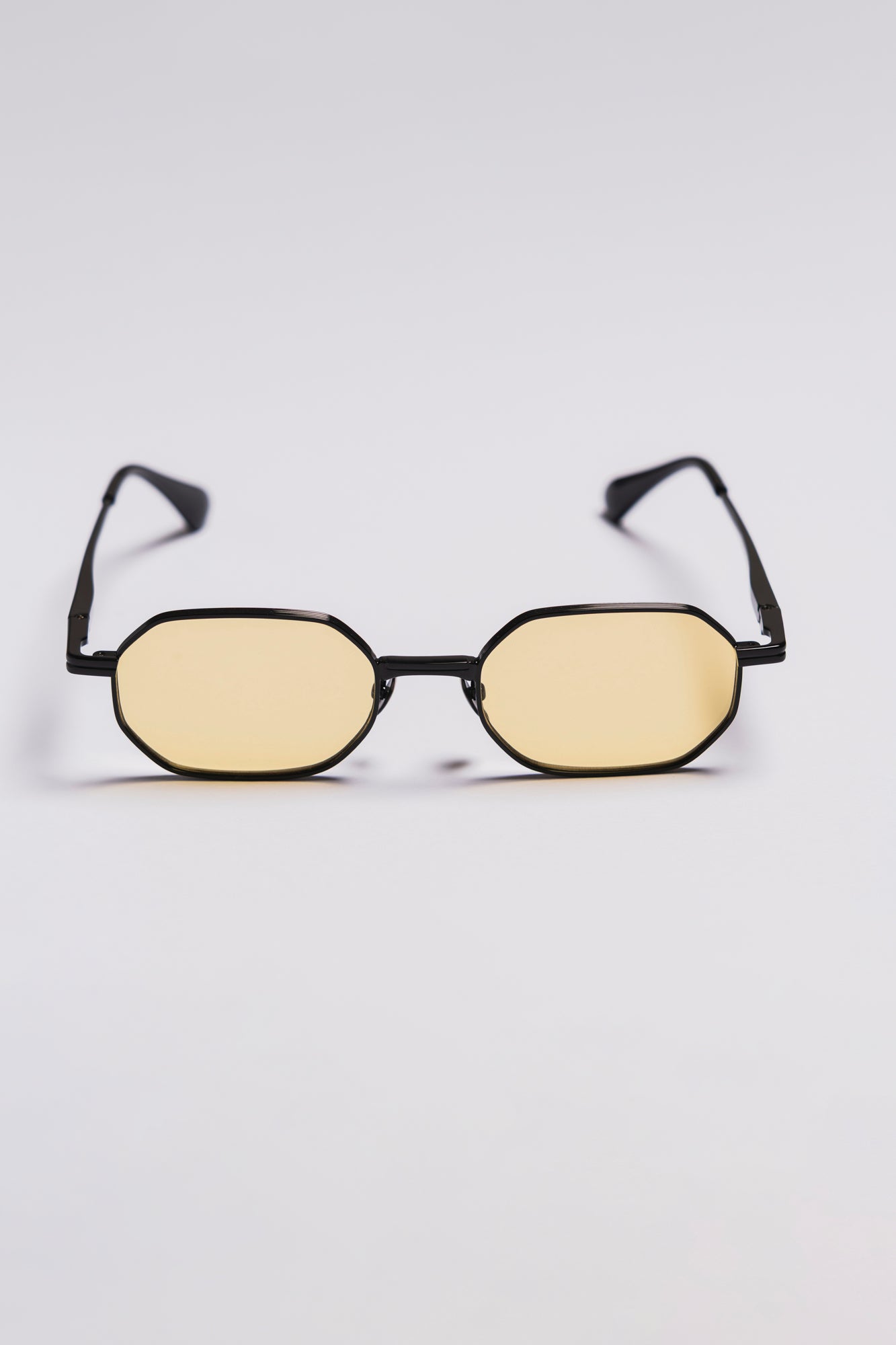 Small oval sunglasses with black frame and yellow lenses on a light gray background