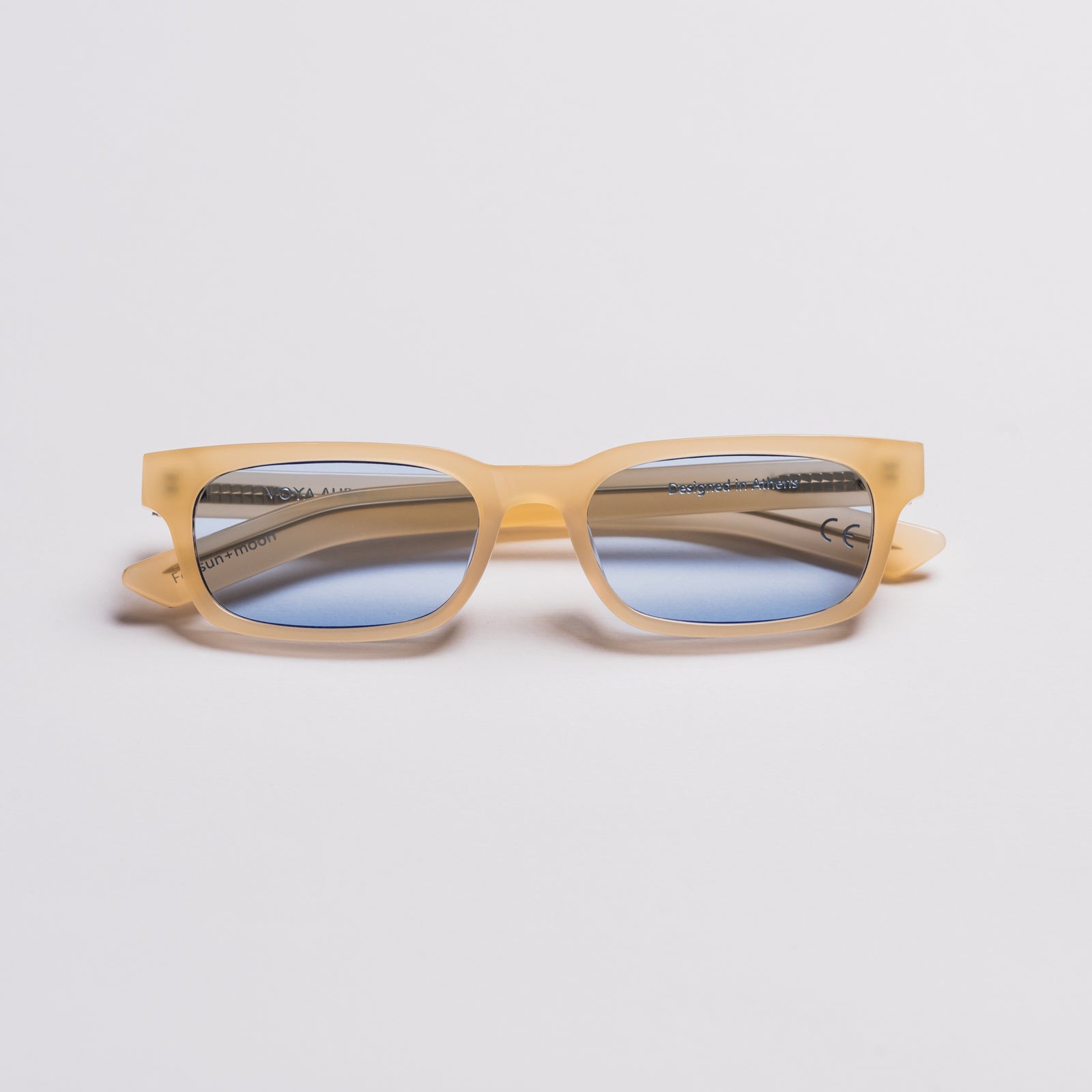 A pair of square-frame sunglasses with translucent light yellow-orange acetate frames and blue mirrored lenses, shown from the side on a light gray background.
