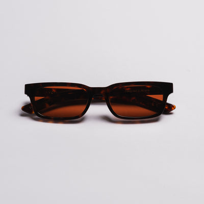 A pair of square-frame sunglasses with dark brown tortoiseshell frames and amber-brown tinted lenses, photographed on a clean light gray background.