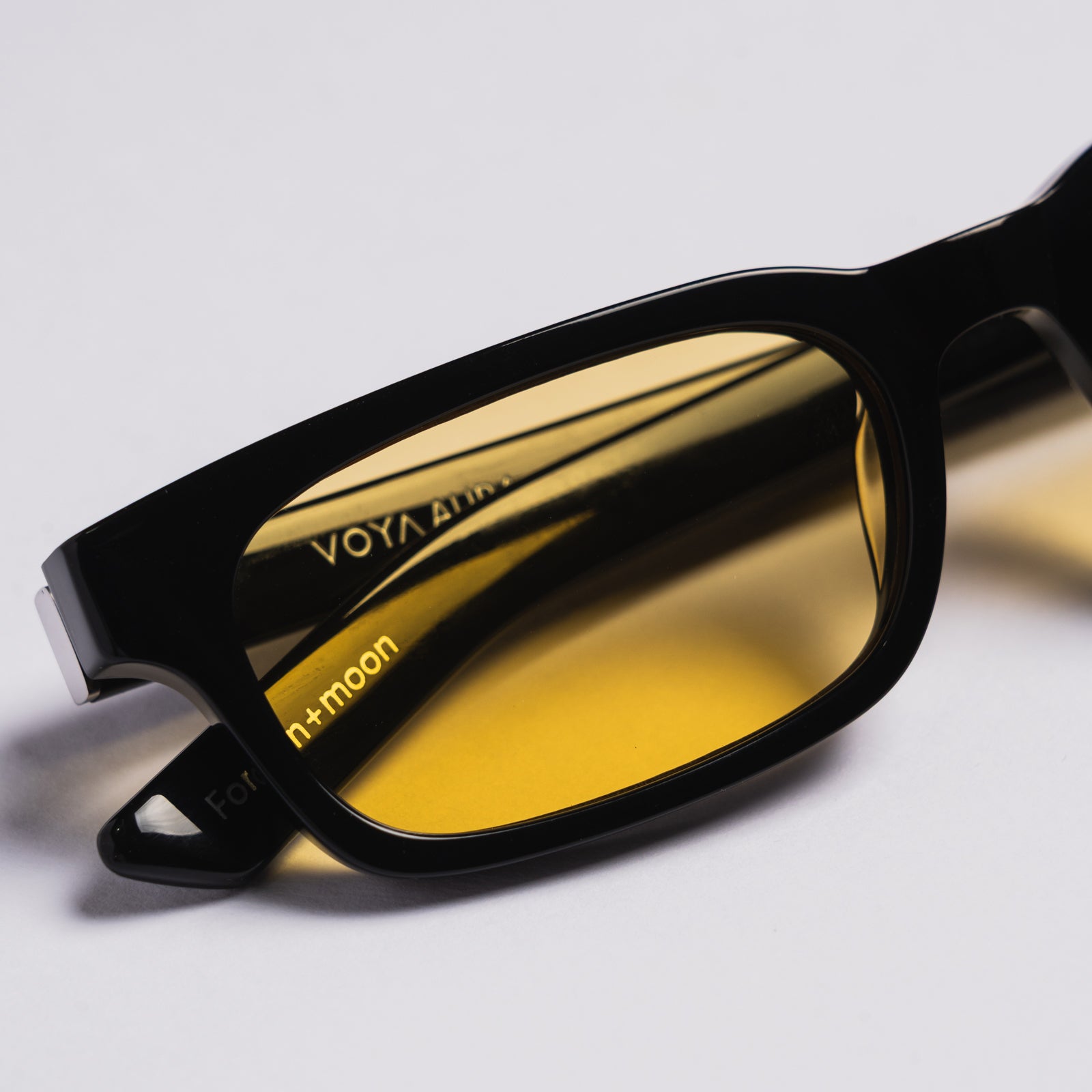 Black rectangular sunglasses with yellow tinted lenses, shown on a clean light gray background. The brand name 'VOYA' is visible on the temple arm.