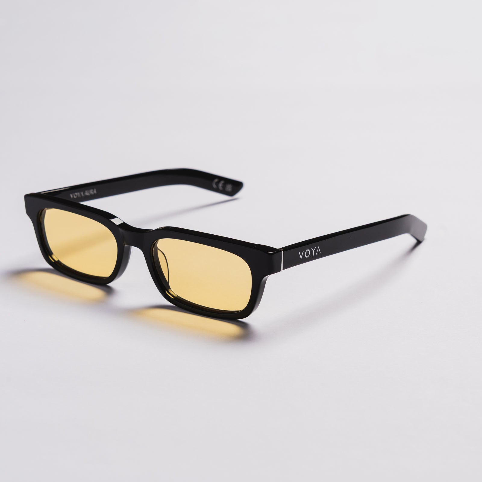 Black rectangular sunglasses with yellow tinted lenses, shown on a clean light gray background. The brand name 'VOYA' is visible on the temple arm.