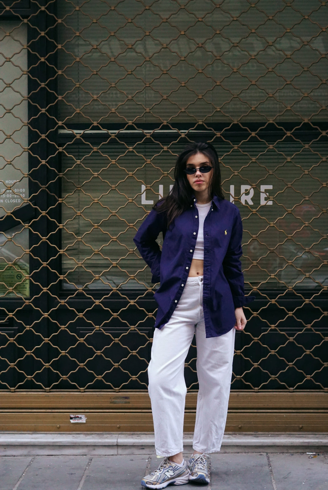 Person wearing a purple jacket and white pants standing in front of a textured wall.