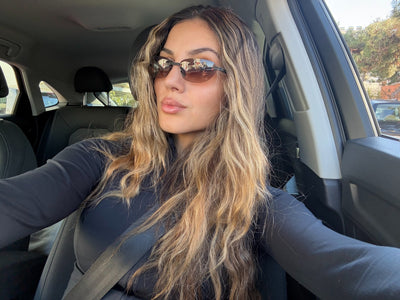 Woman sitting in a car wearing sunglasses and a dark jacket.