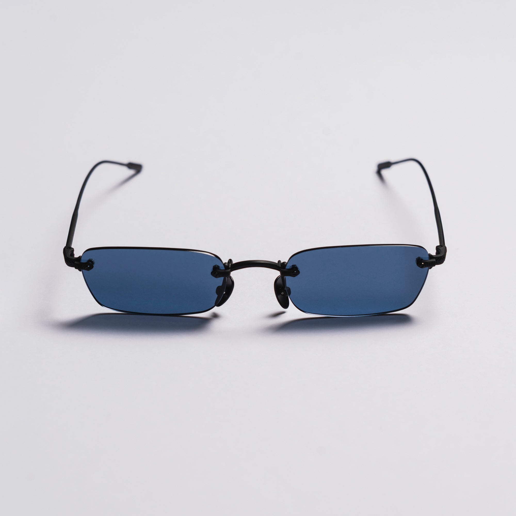 Small rectangular sunglasses with black frames and blue lenses on a light gray background