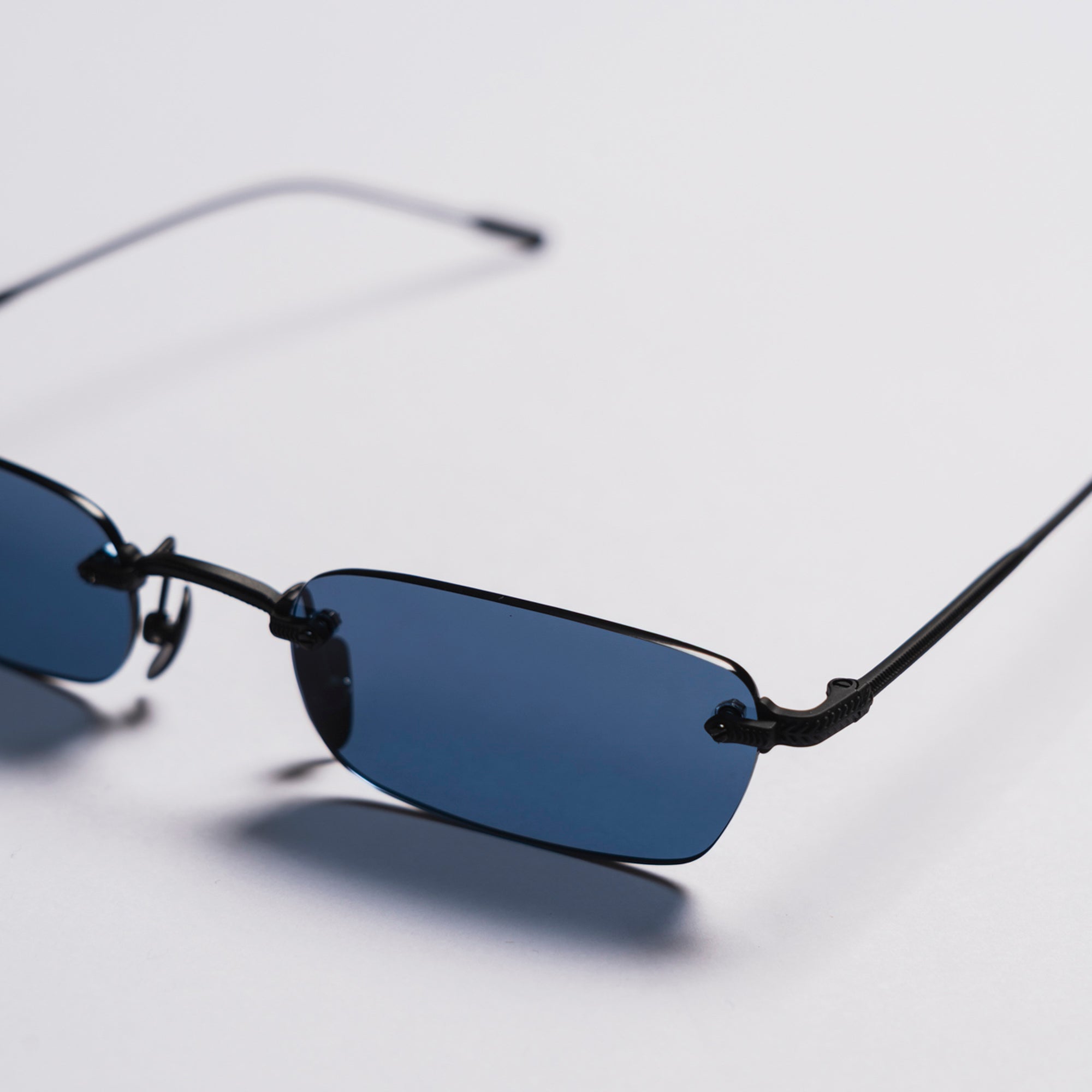 Sunglasses with blue lenses and thin black frames on a light gray background