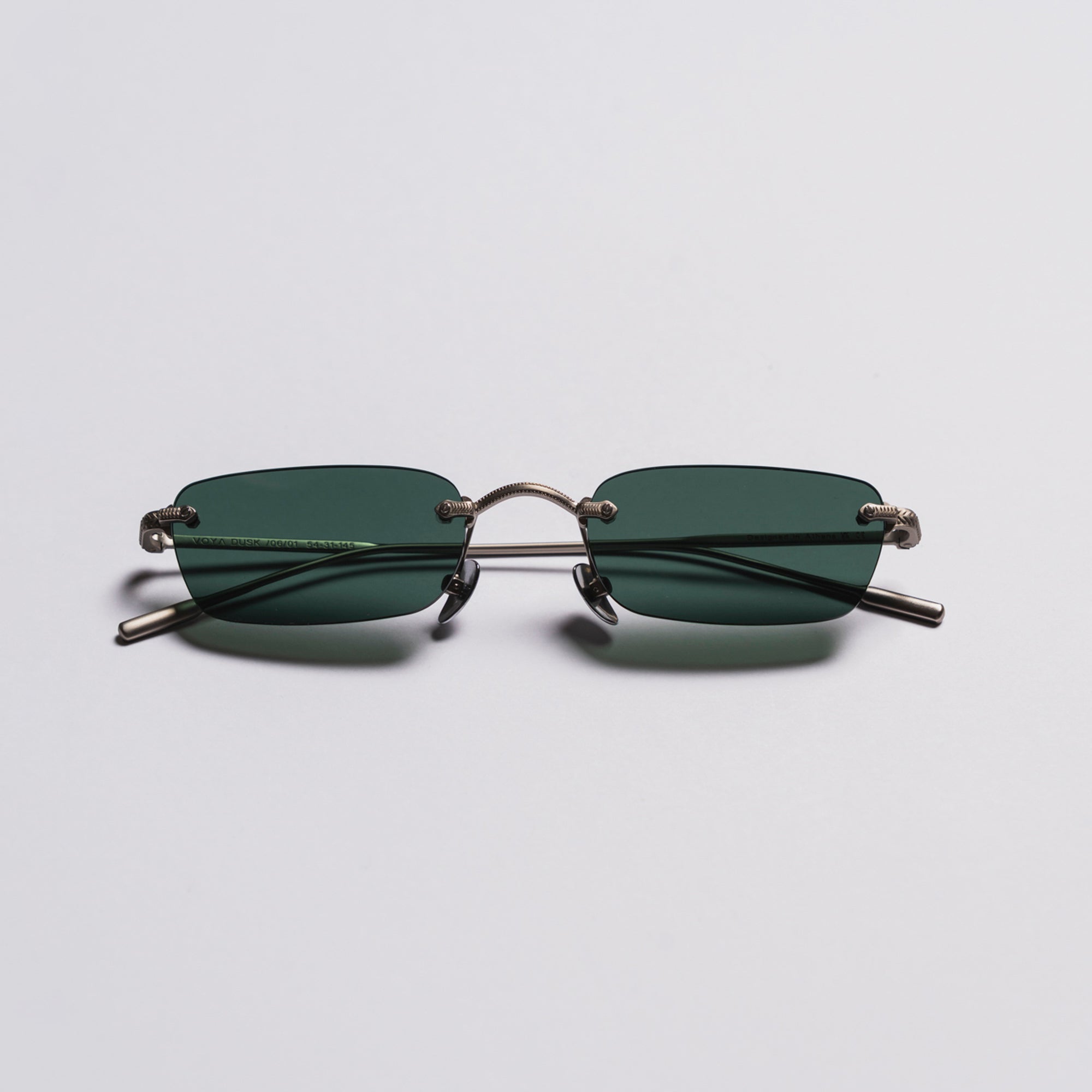 Sunglasses with thin metal frame and green lenses on a light gray background