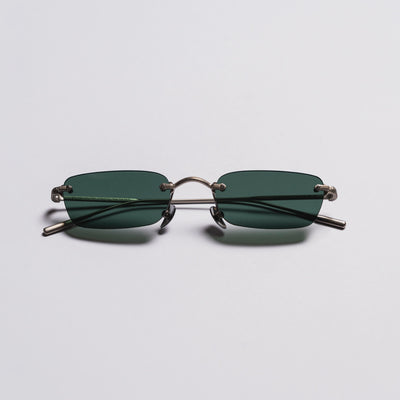 Sunglasses with thin metal frame and green lenses on a light gray background