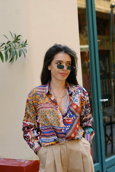 Woman wearing a colorful patterned shirt and sunglasses outdoors.