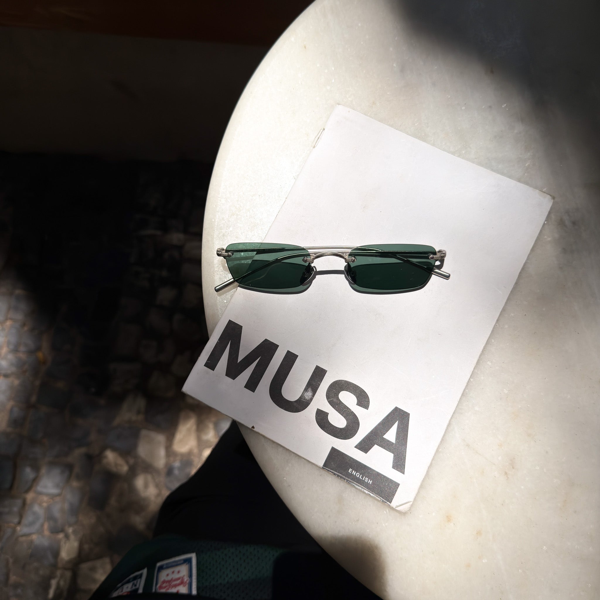 Sunglasses on a white card with 'MUSA' branding on a textured surface.