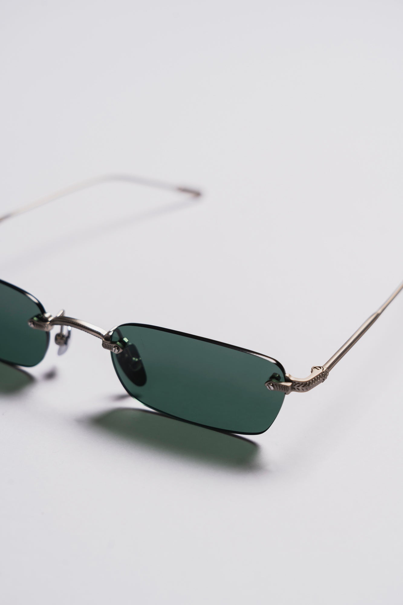 Small green sunglasses with thin metal frame on a light gray background