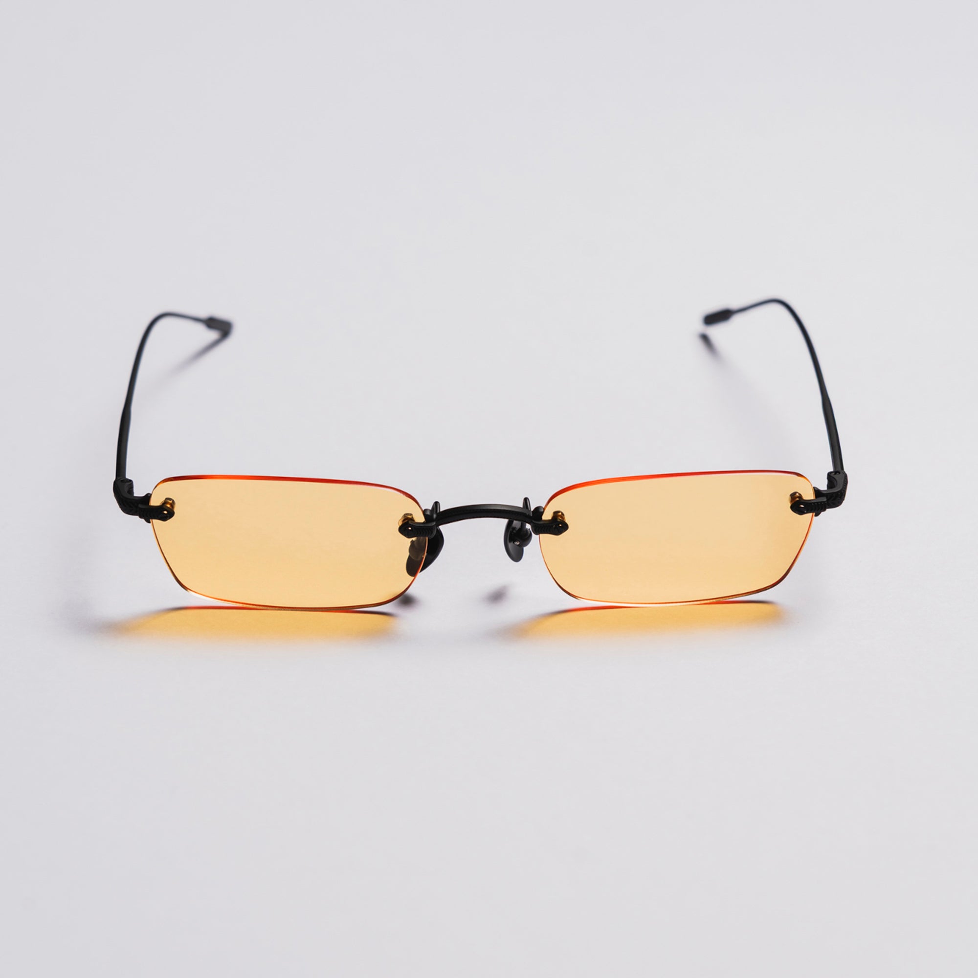 Pair of glasses with yellow lenses and black frames on a light gray background