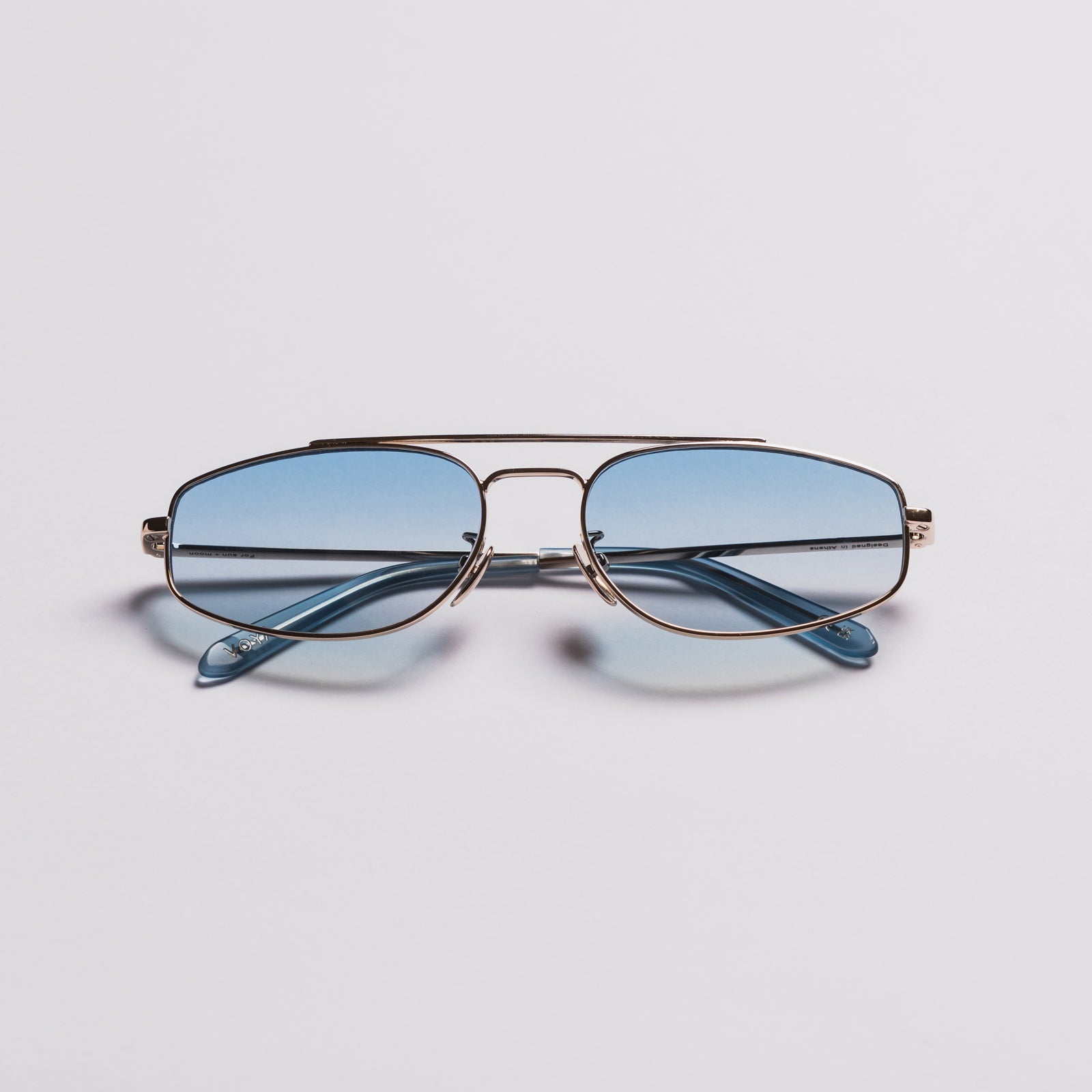 A pair of aviator-style eyeglasses with a thin gold-tone metal frame and light blue tinted lenses, shown on a clean light gray background.