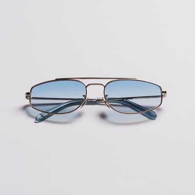 A pair of aviator-style eyeglasses with a thin gold-tone metal frame and light blue tinted lenses, shown on a clean light gray background.