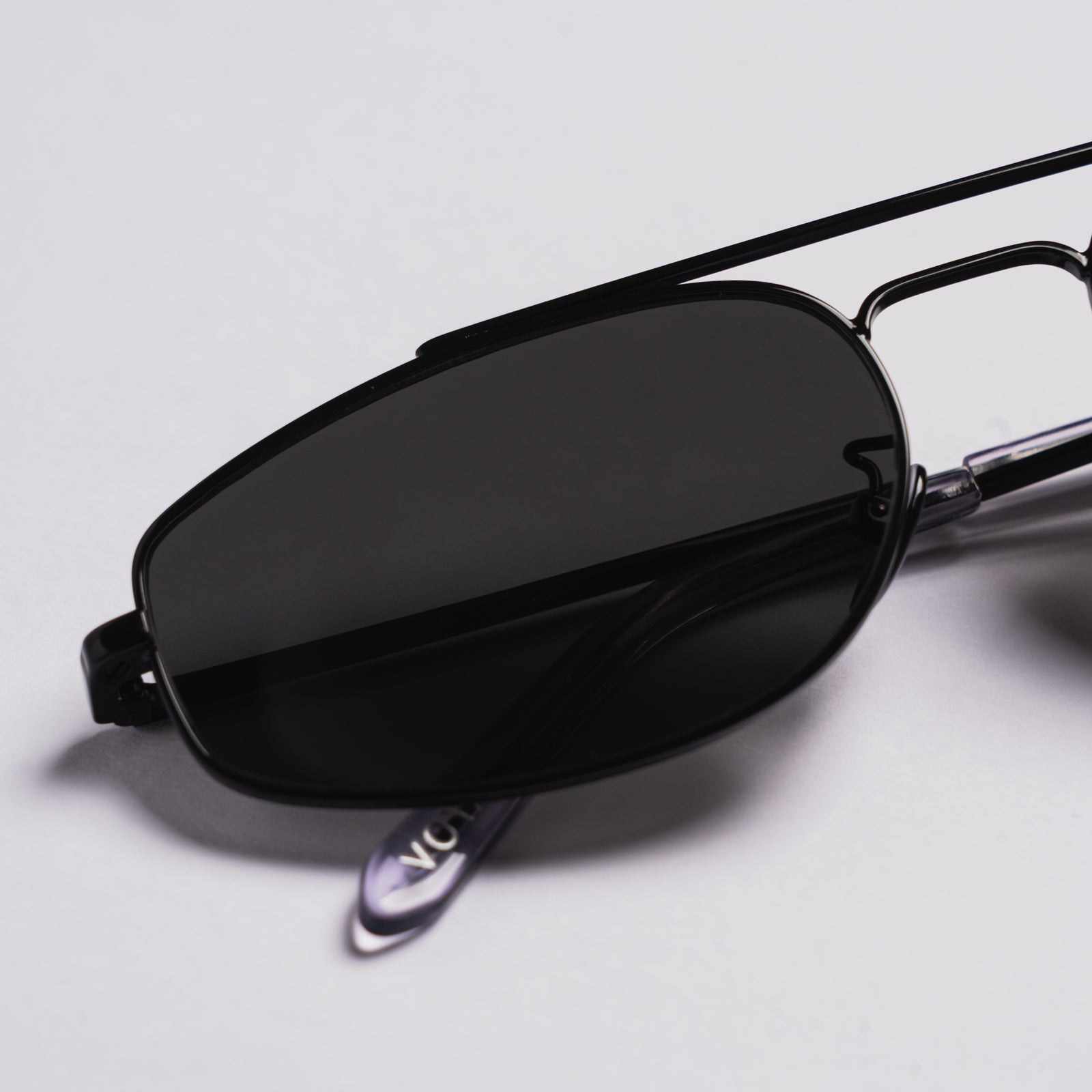 Black metal aviator-style sunglasses with dark tinted lenses, shown resting on a light gray surface.