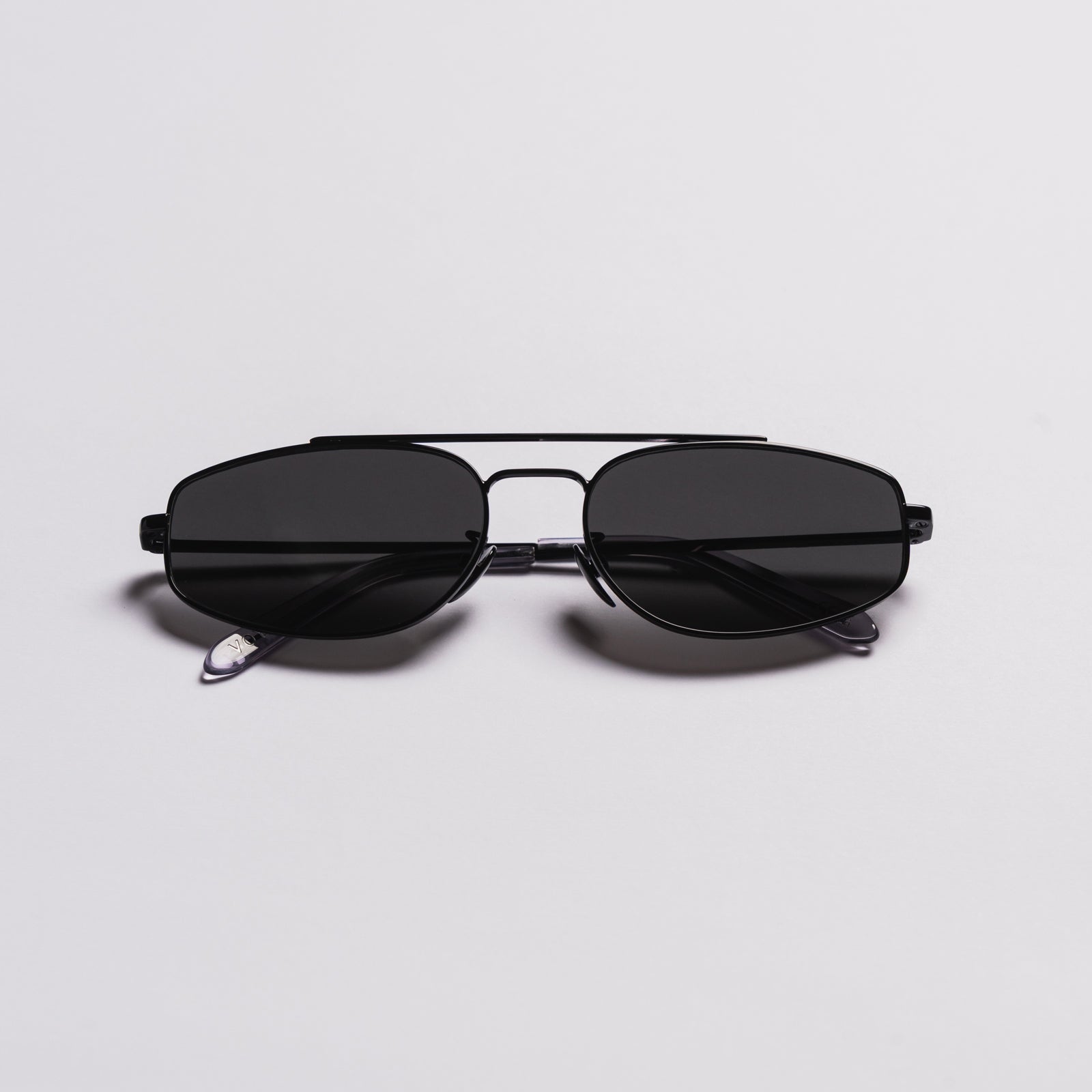 A pair of black aviator-style sunglasses with a double bridge and dark lenses, photographed on a clean light gray background.