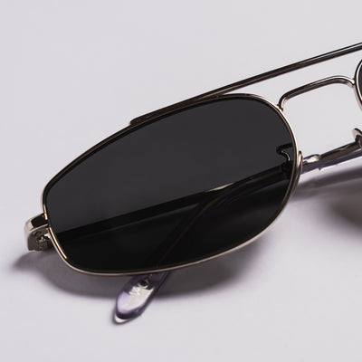 Close-up of a pair of aviator-style sunglasses with dark tinted lenses and a thin metallic frame, photographed on a light gray background.