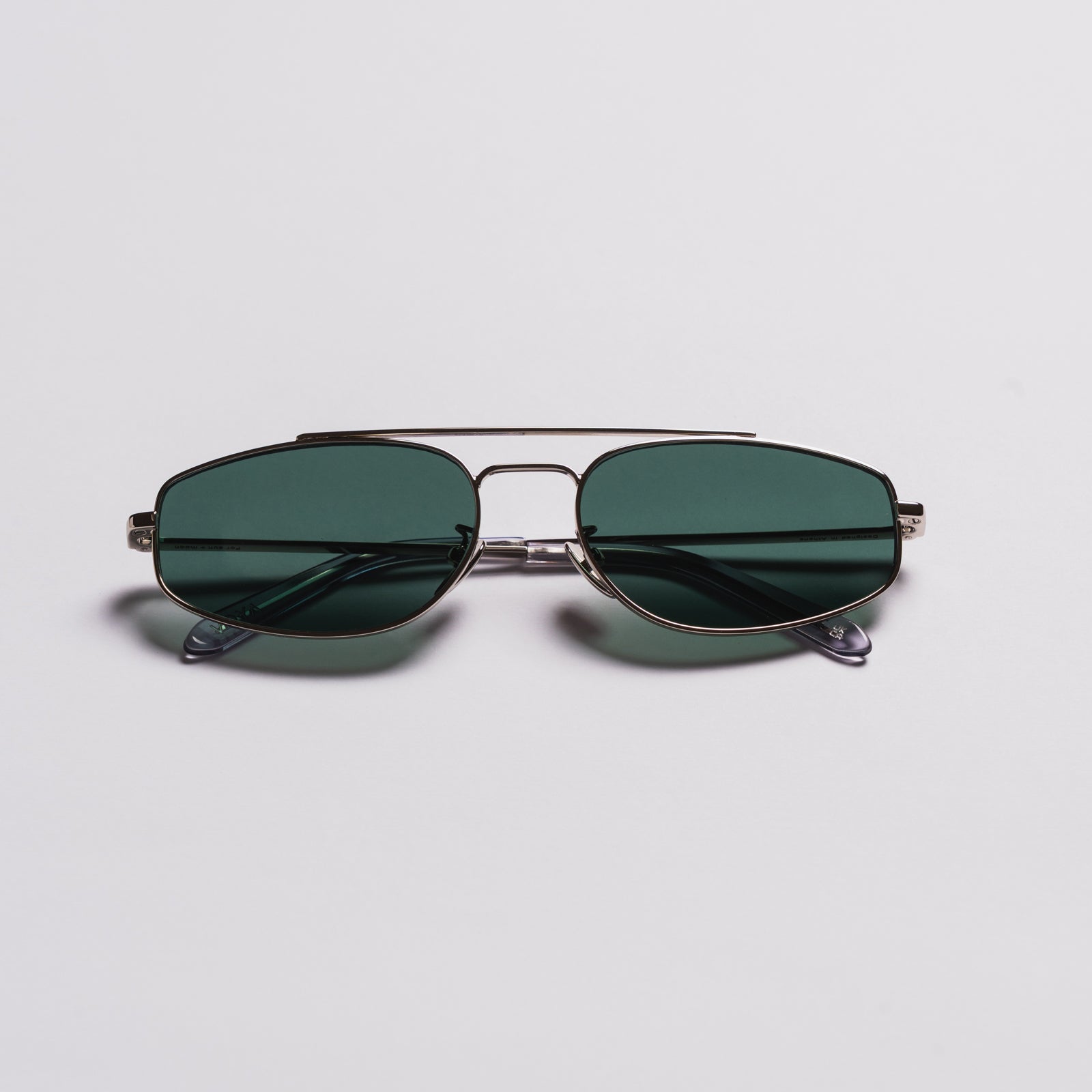 A pair of aviator-style sunglasses with dark green lenses and a thin silver metal frame, displayed on a clean light gray background.