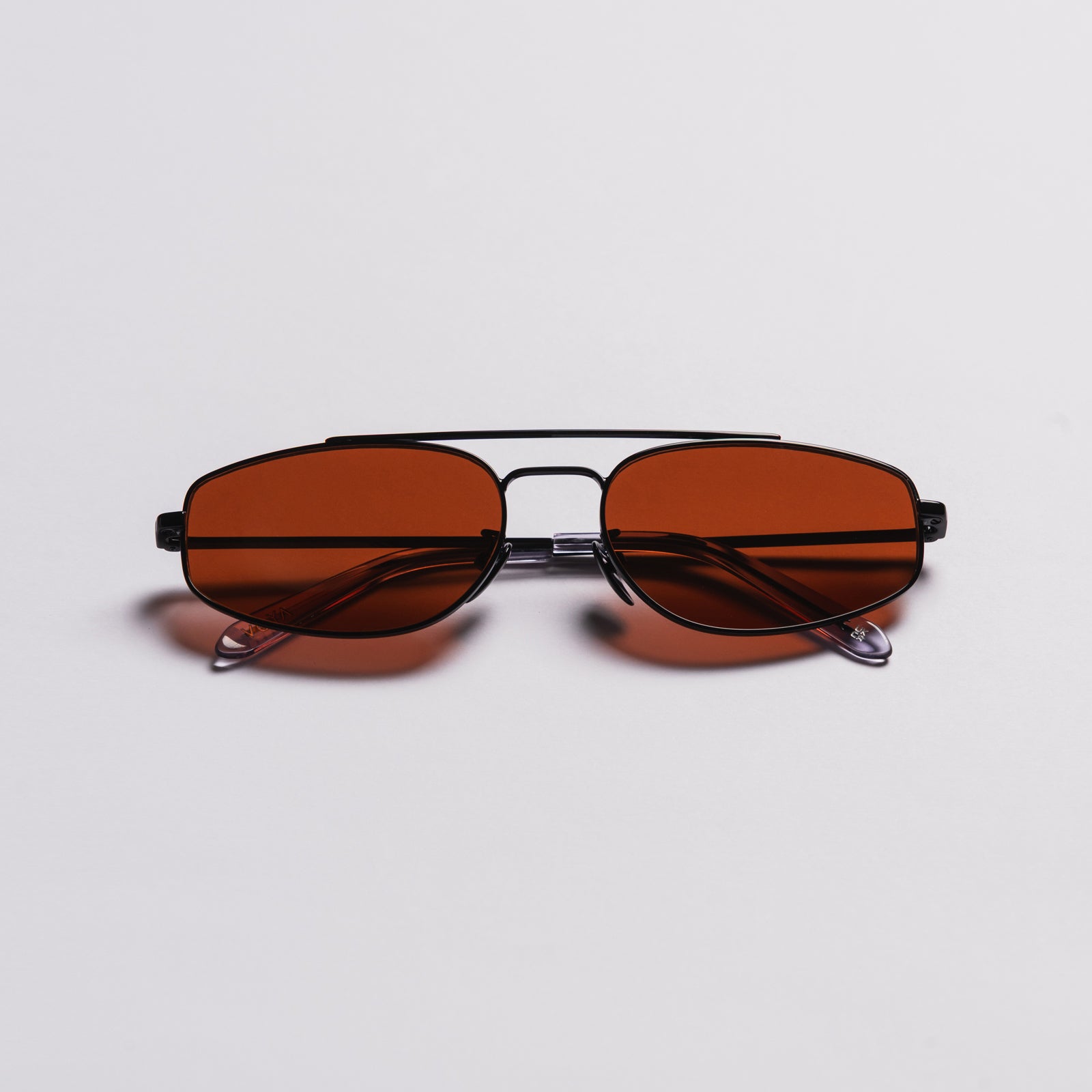 A pair of square aviator-style sunglasses with a black metal frame and warm brown tinted lenses, photographed from the front on a light gray background.