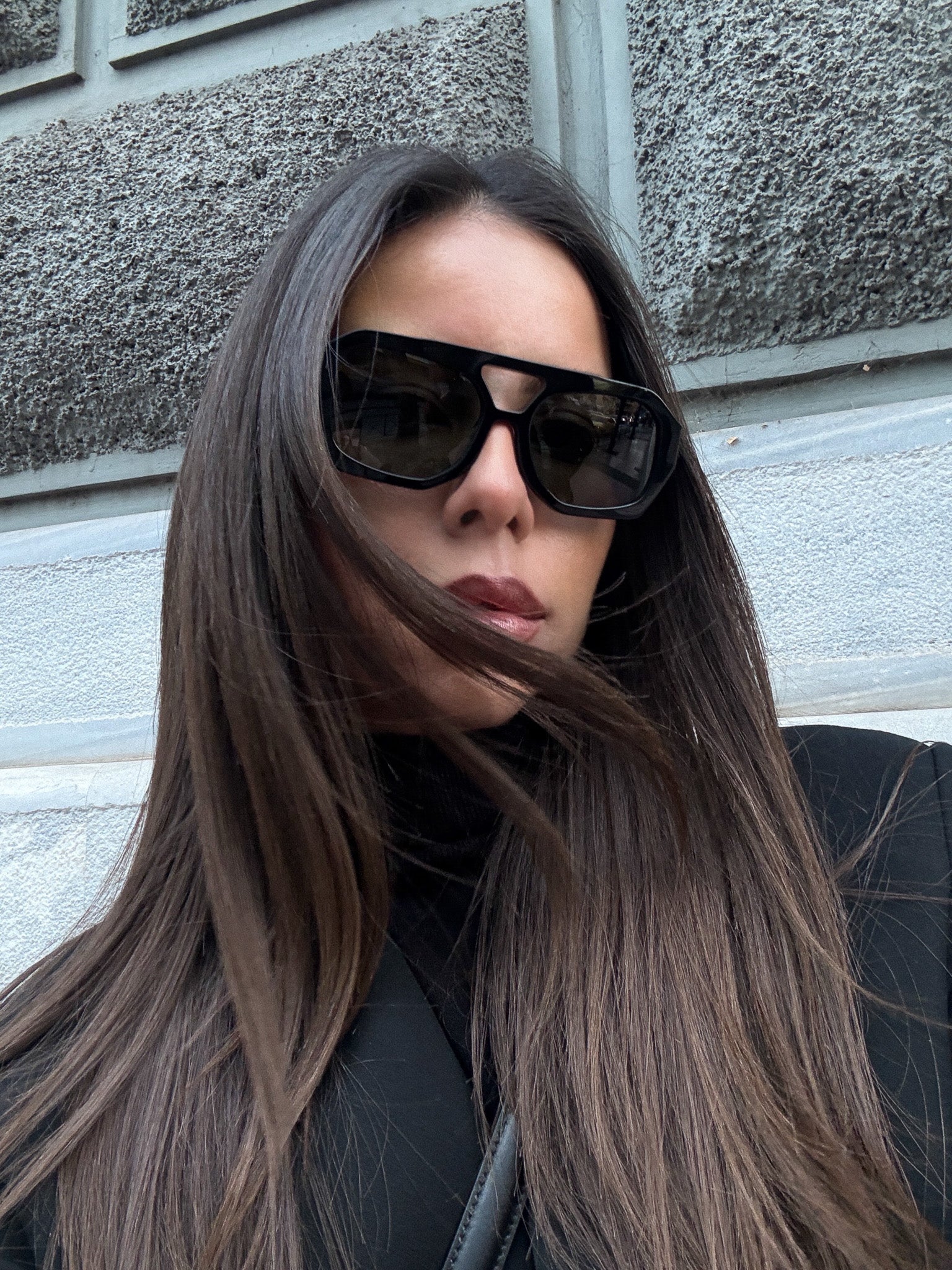Woman wearing sunglasses with a gray wall background