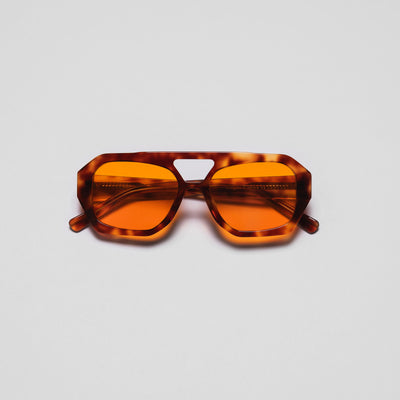 A pair of sunglasses with orange lenses and a patterned frame viewed from a front angle against a white background.