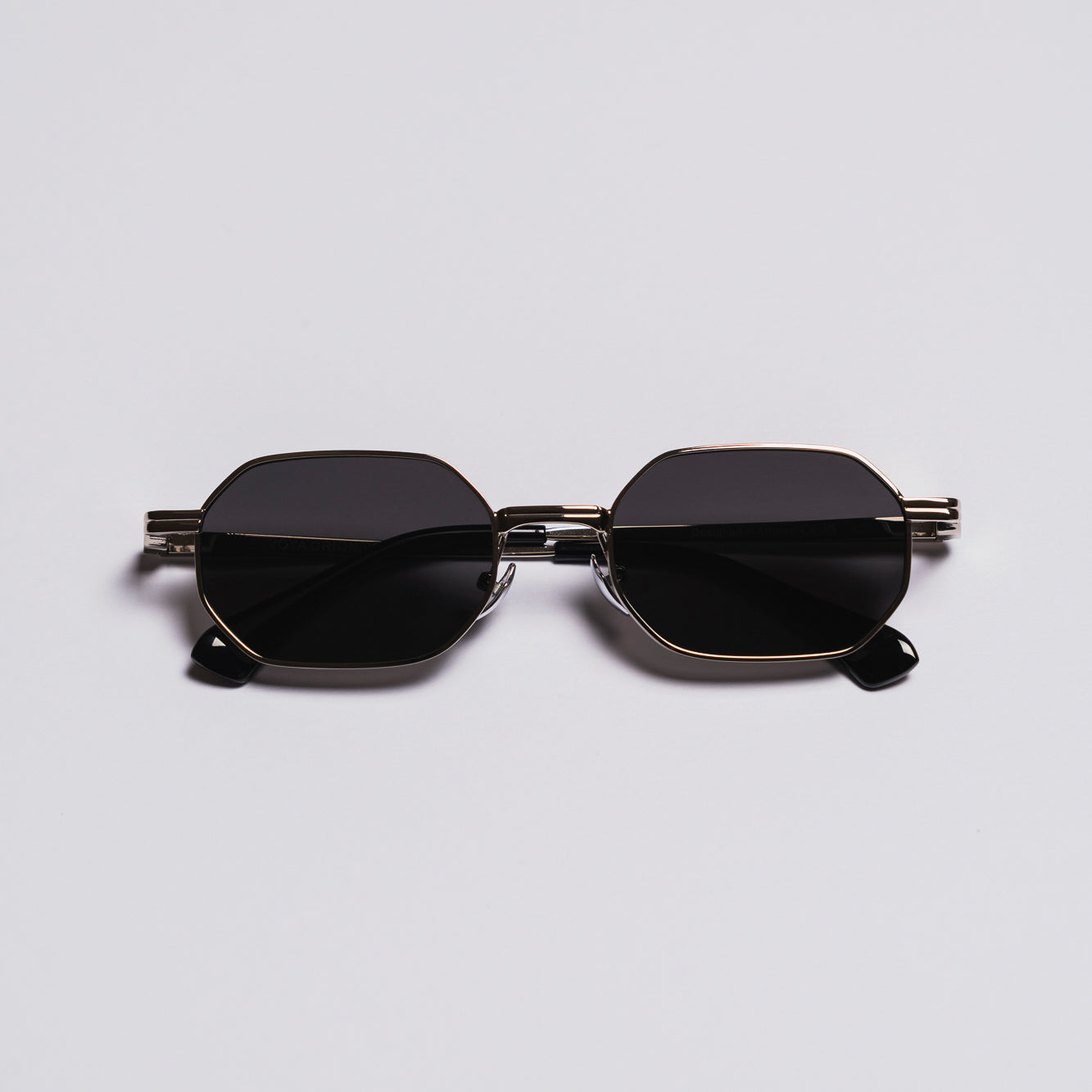 Sunglasses with black lenses and gold frame on a light gray background