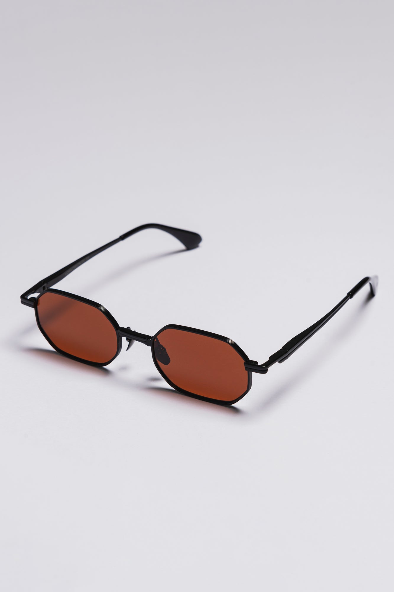 Small oval sunglasses with black frames and brown lenses on a light gray background