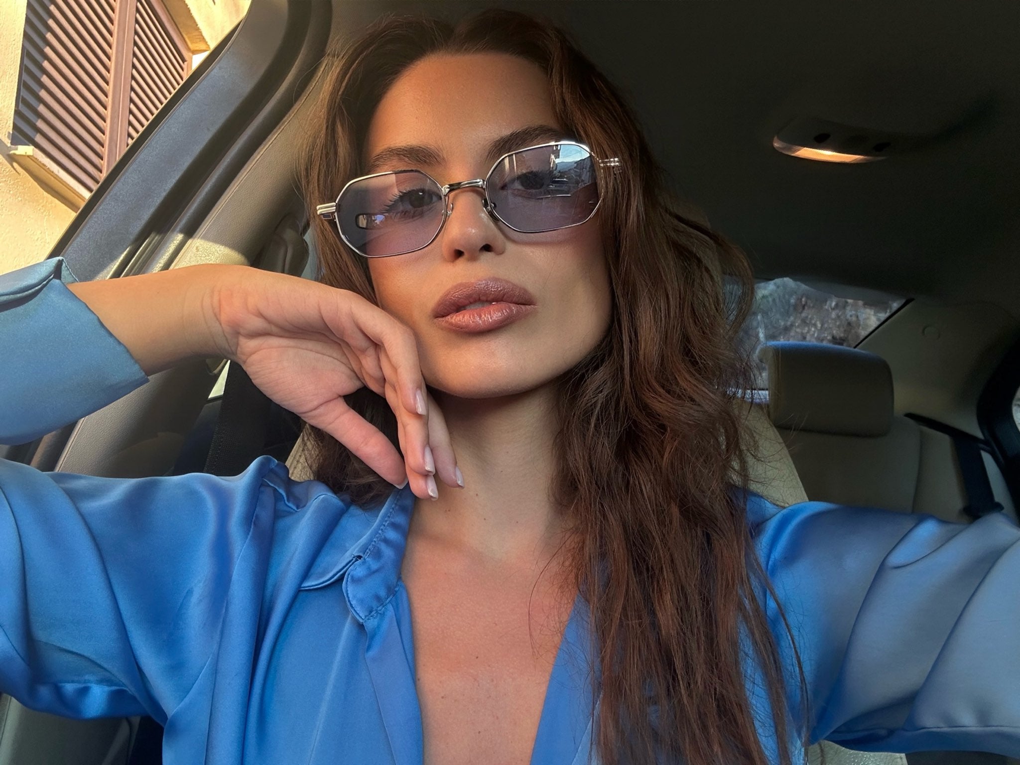 Woman wearing sunglasses and a blue shirt inside a car