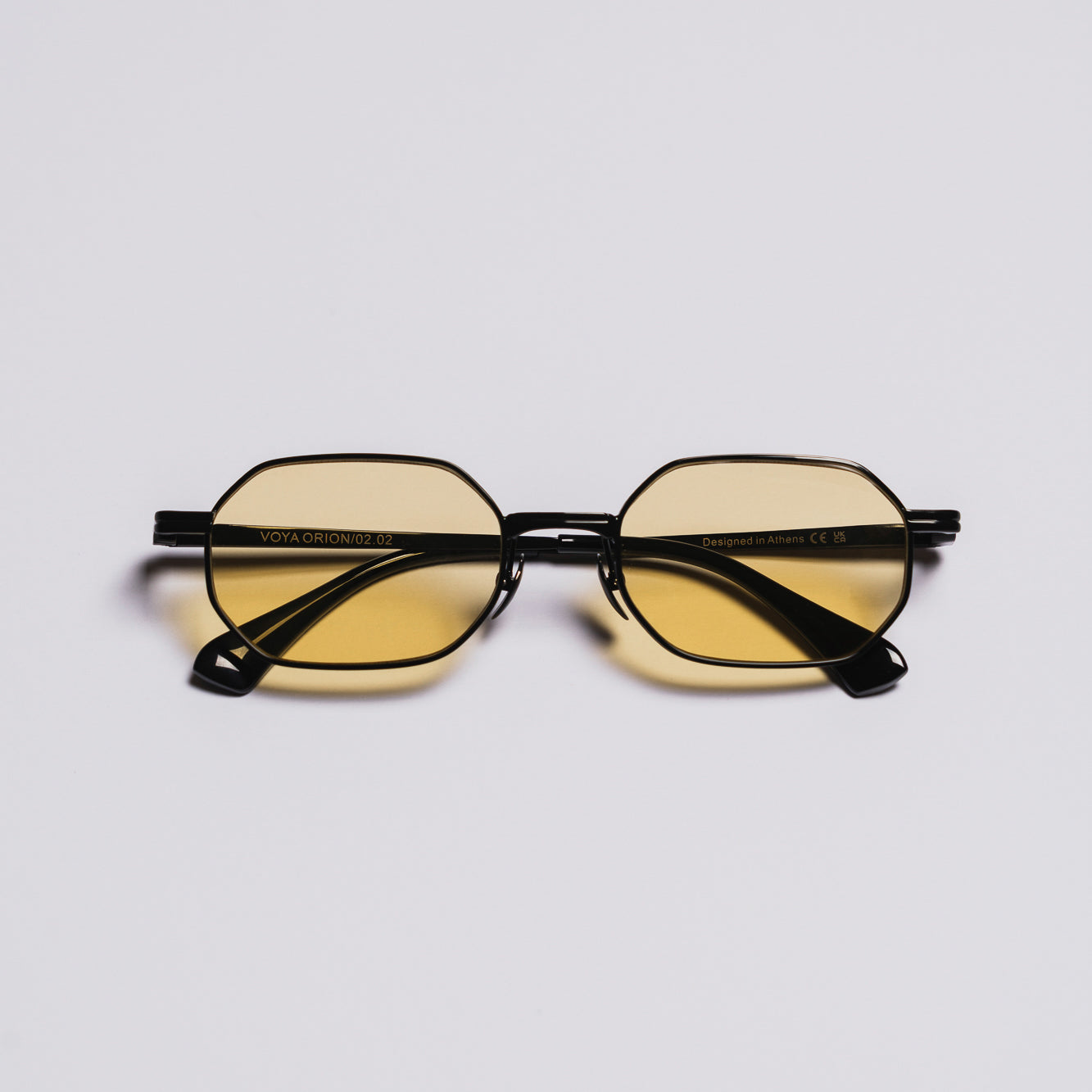 Black-framed sunglasses with yellow-tinted lenses on a light gray background