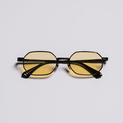 Black-framed sunglasses with yellow-tinted lenses on a light gray background