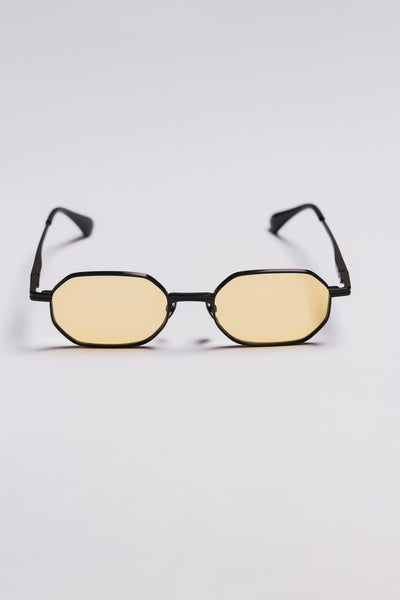 Small oval sunglasses with black frame and yellow lenses on a light gray background