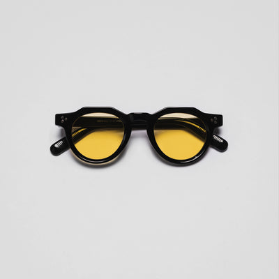 A pair of sunglasses with black frames and yellow tinted lenses on a white background.